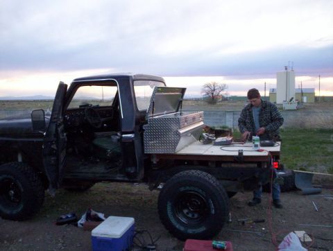1978 Ford Bronco - A person works on the flatbed of a black pickup truck at dusk.