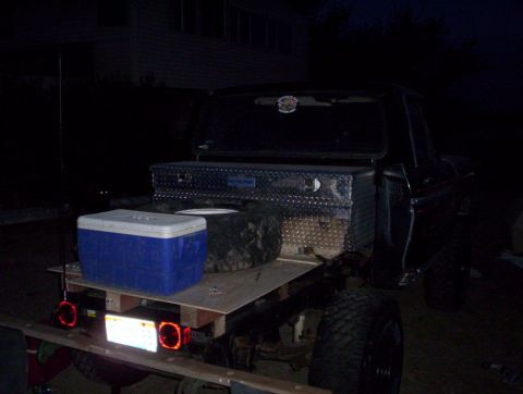 1978 Ford Bronco - A flatbed truck is parked at night, loaded with a cooler and a toolbox.