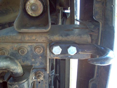 Close-up of a metal tow hook bolted to a vehicle's frame with visible rust and bolts