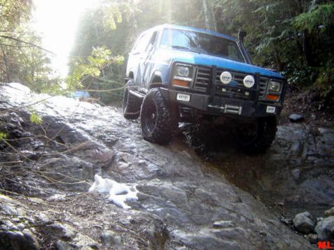 Blue 1985 Ford Bronco off-roading on a rocky trail