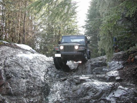 Green Jeep Wrangler driving on a rocky, snowy off-road trail.