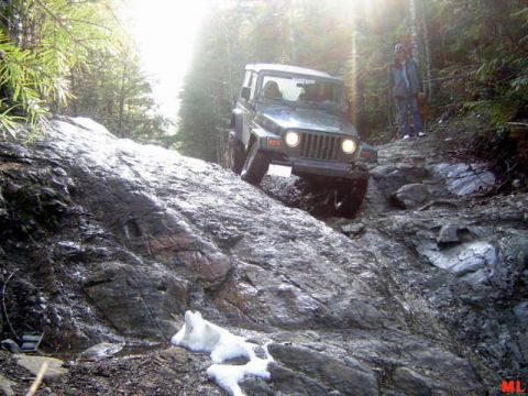 Jeep Wrangler climbing a rocky off-road trail with sun flare.