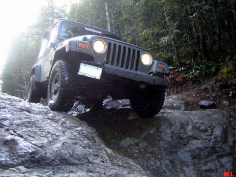 Jeep Wrangler driving over wet rocks on a wooded trail.
