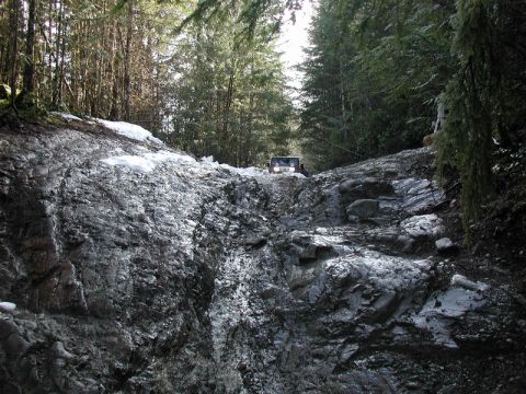 White Jeep Wrangler climbing a difficult rocky and muddy trail with snow.