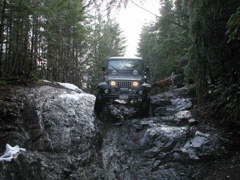 Jeep Wrangler driving on a rocky, snowy off-road trail in a forest.
