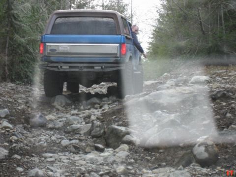 Blue Ford Bronco driving on a rocky trail, person leaning out window.