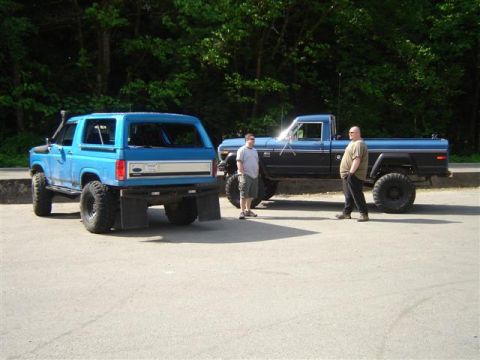 Blue Ford Bronco and blue Ford pickup truck parked with two men standing nearby.
