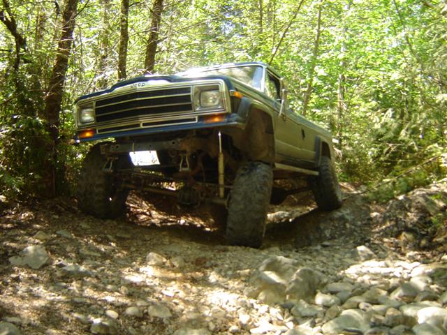 Lifted green Jeep Cherokee on a rocky, wooded trail.