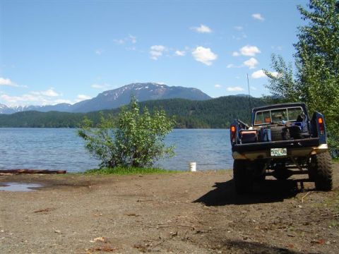 Blue Ford pickup truck parked by a lake with mountains in the background.