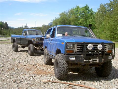 Lifted blue Ford Bronco and pickup truck on gravel lot