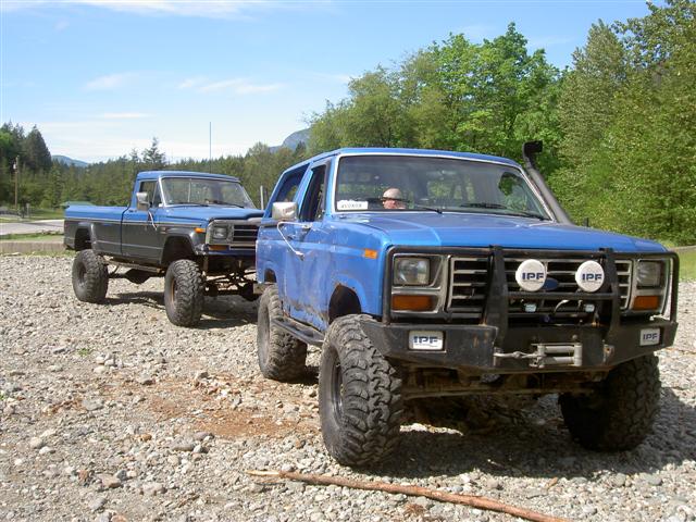 Lifted blue Ford Bronco and pickup truck on gravel lot