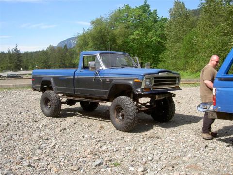 Lifted blue and black pickup truck with off-road tires parked on gravel.