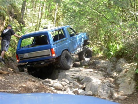 Blue Ford Bronco off-roading on a rocky trail in a forest.