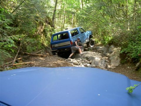 Blue Ford Bronco off-roading on a rocky, wooded trail.