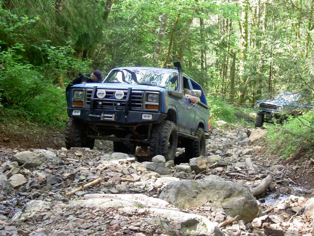 Blue Ford Bronco off-roading on a rocky, wooded trail.