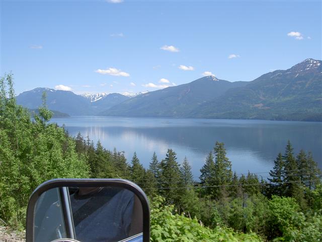 Side mirror reflecting driver with lake and mountain view.