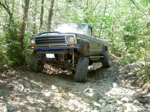 Lifted dark blue Jeep Cherokee on a rocky, wooded trail.