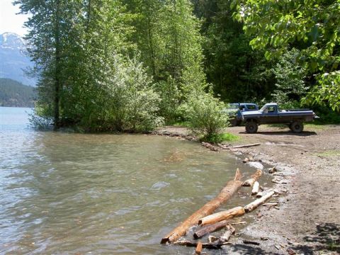 Blue Ford pickup truck parked on a dirt shore by a lake, with a blue SUV behind it.
