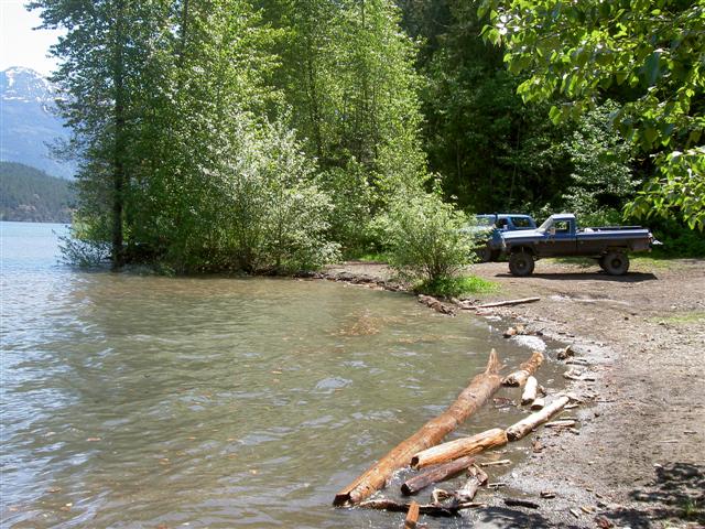 Blue Ford pickup truck parked on a dirt shore by a lake, with a blue SUV behind it.