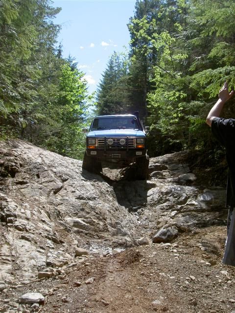 Blue Ford Bronco driving on a rocky off-road trail.