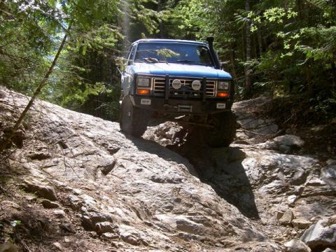 Blue 1985 Ford Bronco climbing a rocky off-road trail