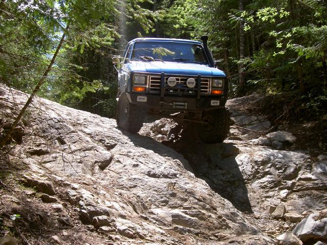Blue 1985 Ford Bronco climbing a rocky off-road trail