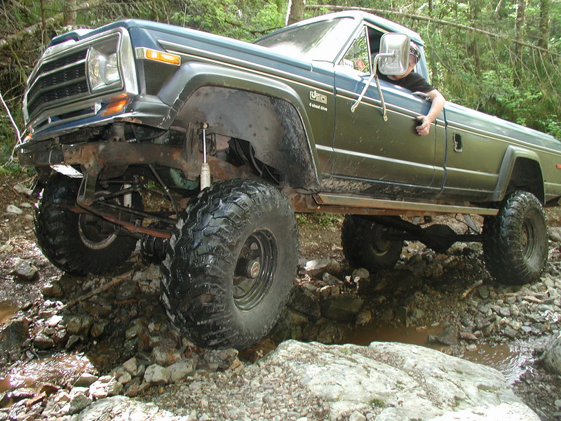 Lifted blue Jeep Comanche pickup truck off-roading on a rocky, wet trail.