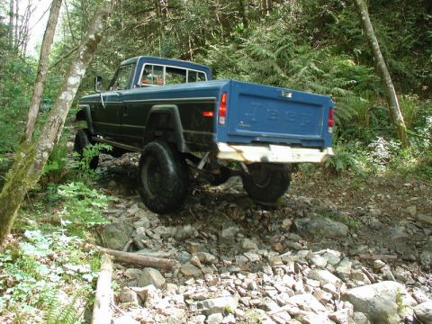 Blue Jeep pickup truck on a rocky, wooded trail.