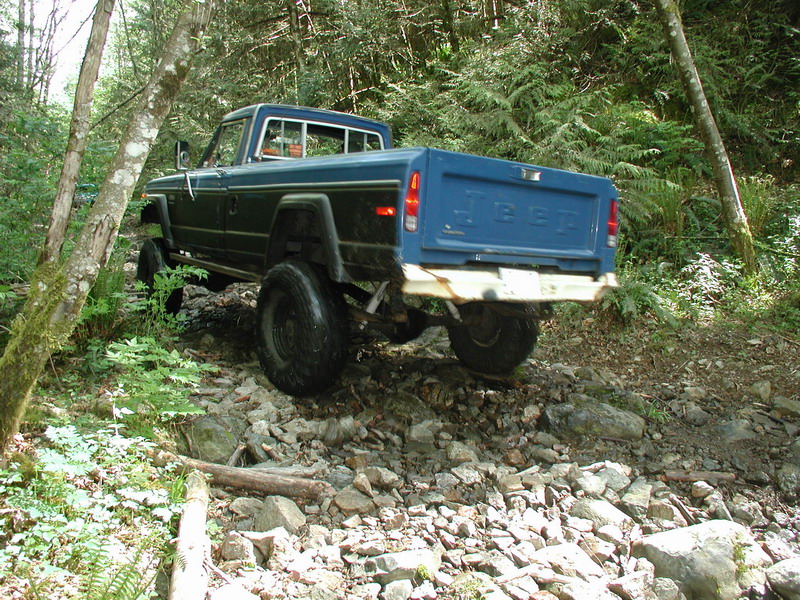 Blue Jeep pickup truck on a rocky, wooded trail.