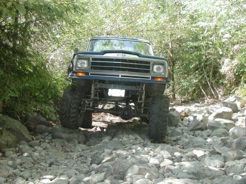 Blue Jeep off-roading on a rocky trail surrounded by trees.