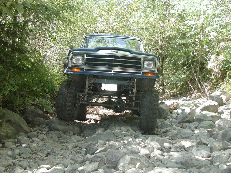 Blue Jeep off-roading on a rocky trail surrounded by trees.