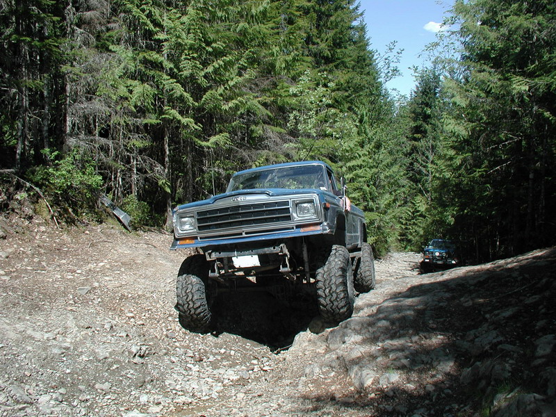 Lifted blue pickup truck on a rocky forest trail.