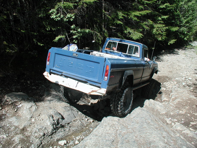 Blue Jeep pickup truck driving on a rocky off-road trail.