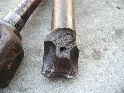 Close-up of two damaged metal vehicle drivetrain parts on concrete.