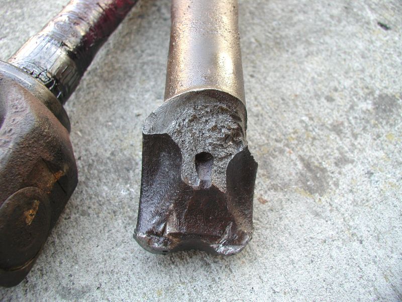 Close-up of two damaged metal vehicle drivetrain parts on concrete.