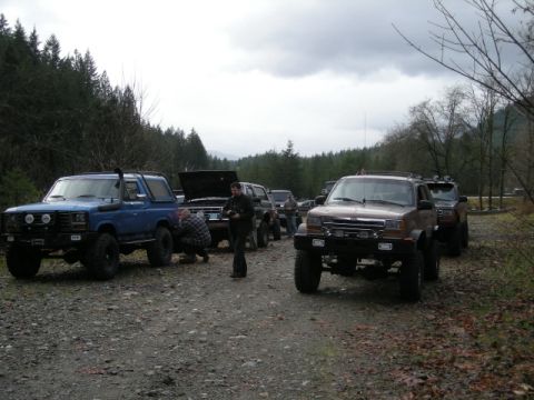 Blue 1980s Ford Bronco in a line of SUVs on a gravel road.
