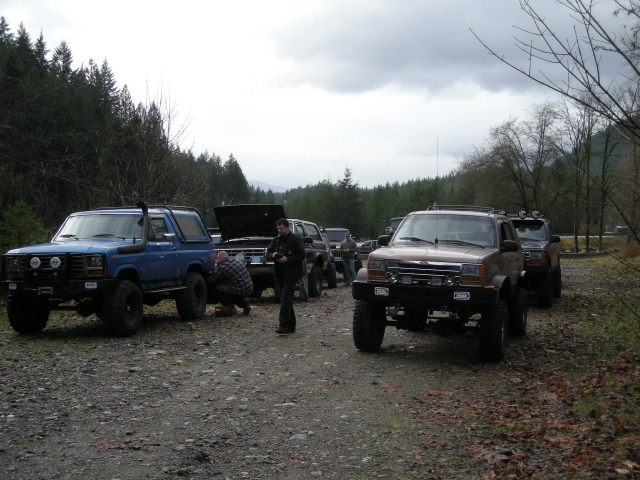 Blue 1980s Ford Bronco in a line of SUVs on a gravel road.