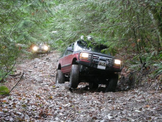 Red SUV driving on a muddy forest trail.