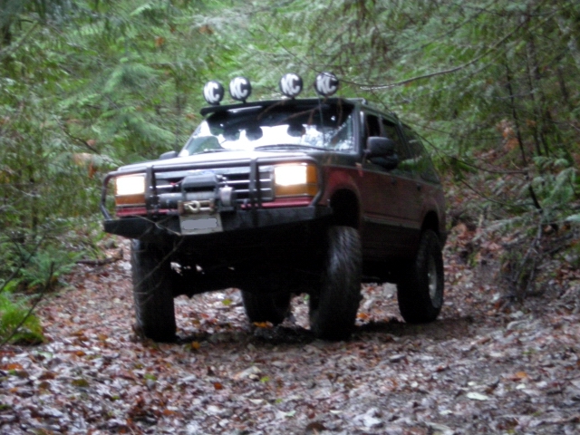 Dark red SUV with winch and KC lights on roof rack driving on forest trail