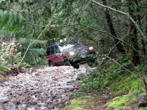 Red SUV driving on a rocky, wooded trail.