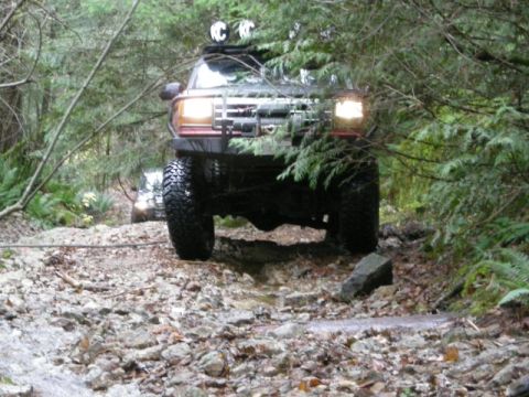 Dark SUV with off-road tires and winch driving on a rocky forest trail.