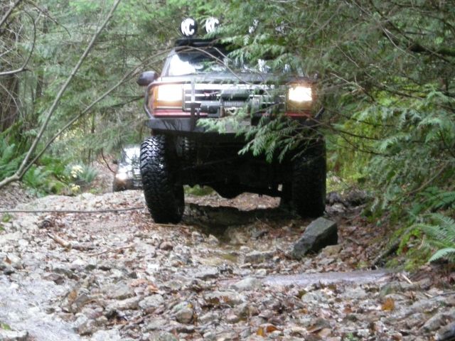 Dark SUV with off-road tires and winch driving on a rocky forest trail.