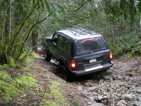 Dark gray Toyota Land Cruiser driving on a rocky, wooded trail.