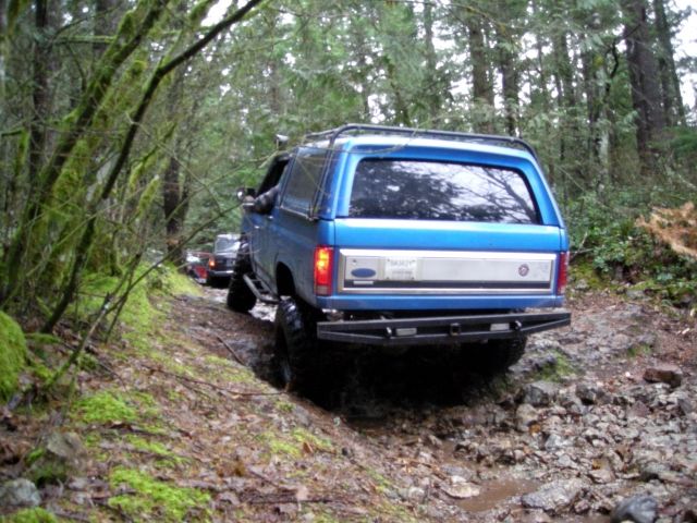 Blue Ford Bronco off-roading on a muddy forest trail.