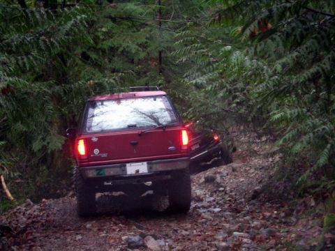 Red Ford SUV driving on a rocky, wooded trail.
