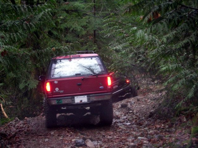 Red Ford SUV driving on a rocky, wooded trail.