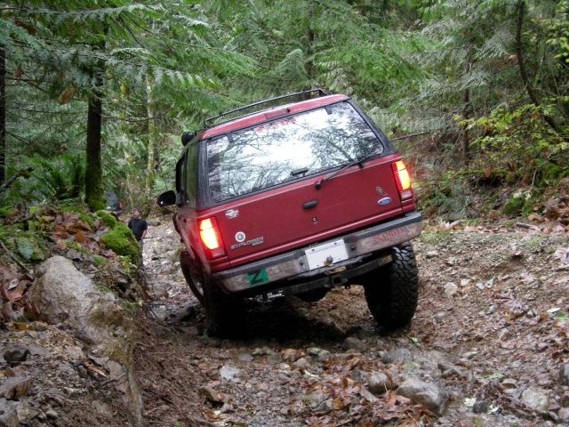 Red Ford Explorer off-roading on a rocky trail in a forest.