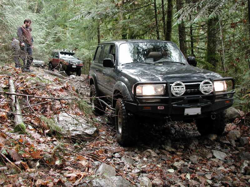 Dark Toyota Land Cruiser off-roading on a rocky, wooded trail.