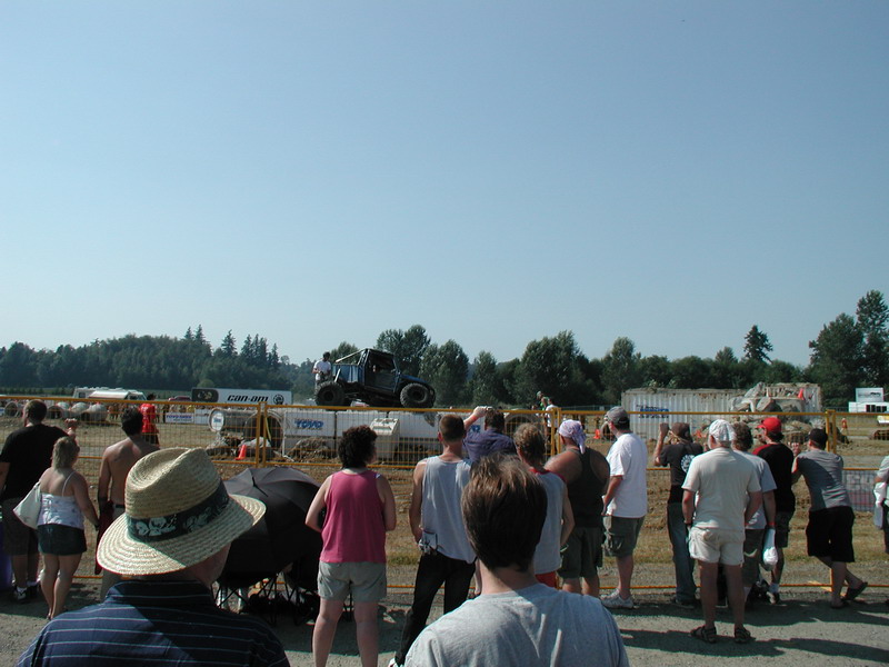 Custom buggy airborne over a dirt track with spectators.