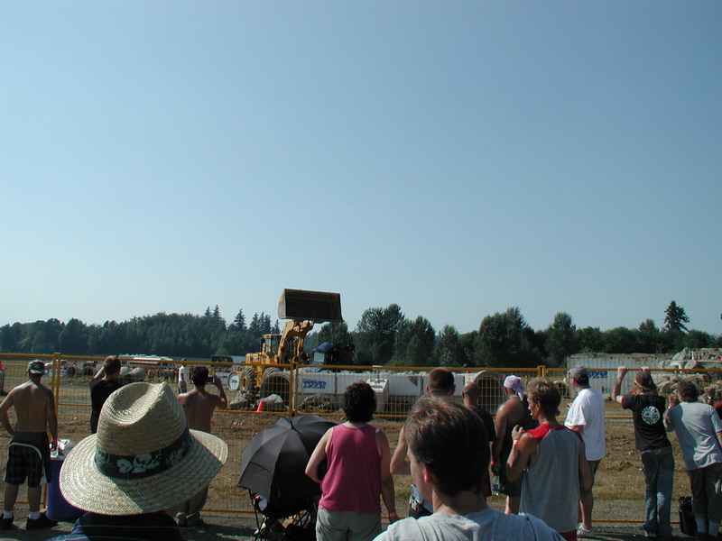Crowd watching a yellow excavator at a construction site.